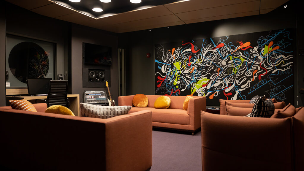 Lounge with orange couches and velvet pillows with abstract black, white, red, green, and orange mural in the background