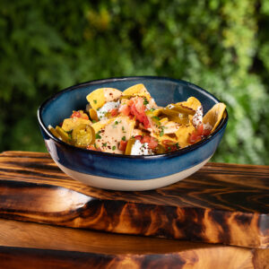 Nachos in large ceramic bowl on wood tray.